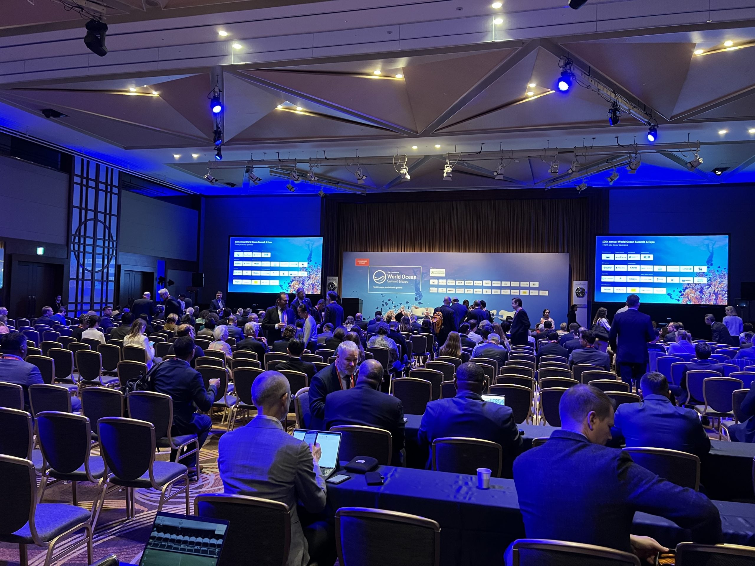 Konferenz-Saal mit Monitoren, Bühne und vielen Teilnehmern
