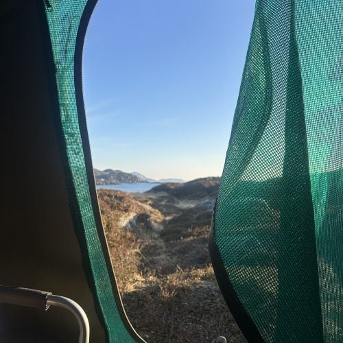 Blick aus einer Zeltöffnung in hügelige Landschaft, im Hintergrund das Meer