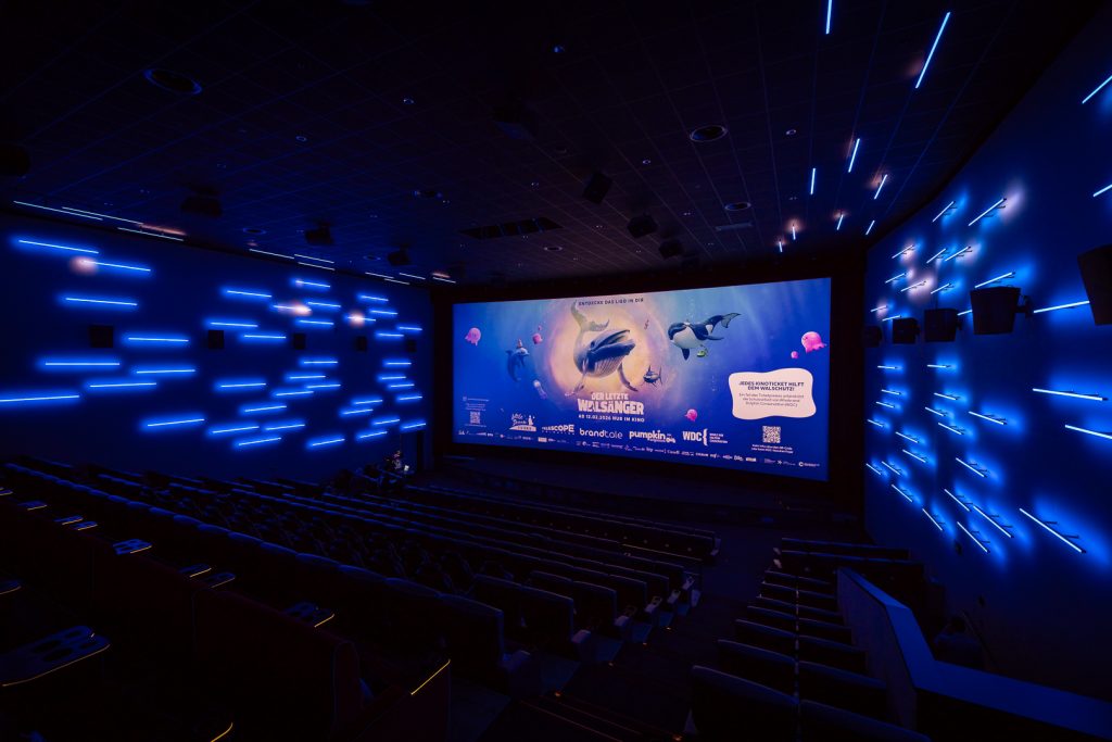 Kinosaal mit aufwendiger bläulicher Beleuchtung; auf der Leinwand ein Wal-Animationsfilm