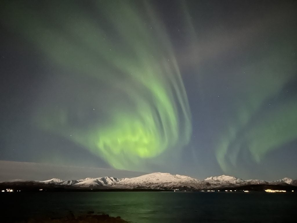 Polarlilchter am Himmel über Gebirgskette und Meer