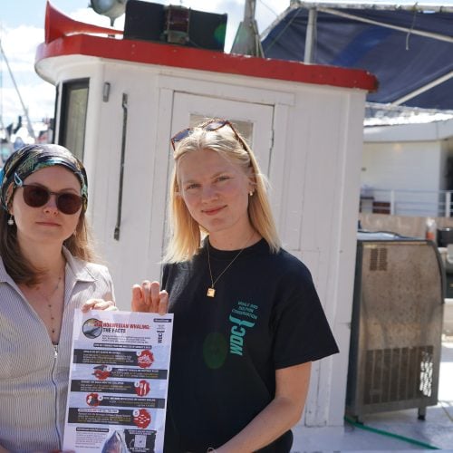 Zwei Frauen am Hafen halten einen DIN-A4-Blatt in die Kamera
