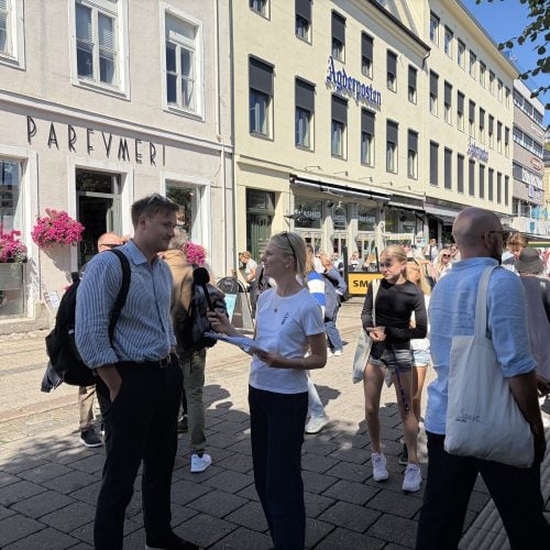Junge Frau interviewt einen Passanten in einer Fußgängerzone.