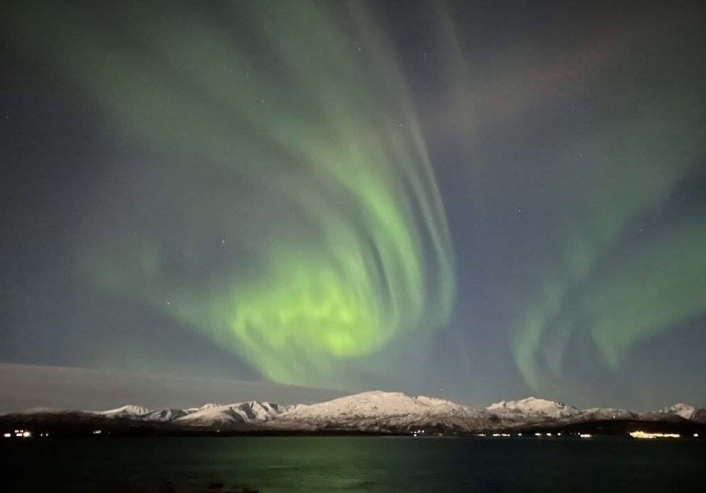 Polarlilchter am Himmel über Gebirgskette und Meer