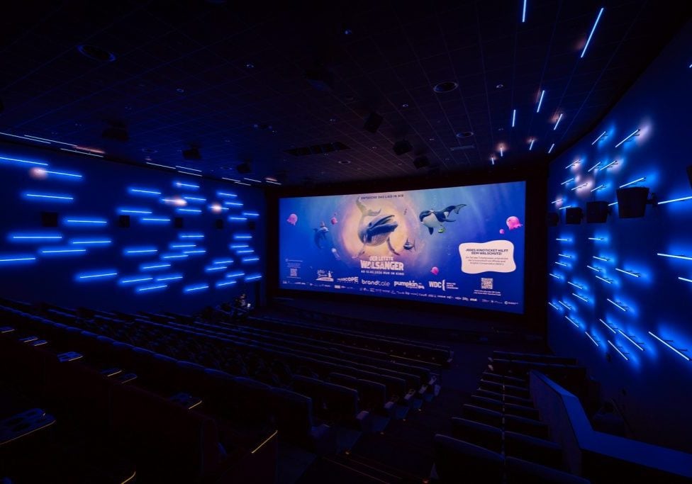 Kinosaal mit aufwendiger bläulicher Beleuchtung; auf der Leinwand ein Wal-Animationsfilm
